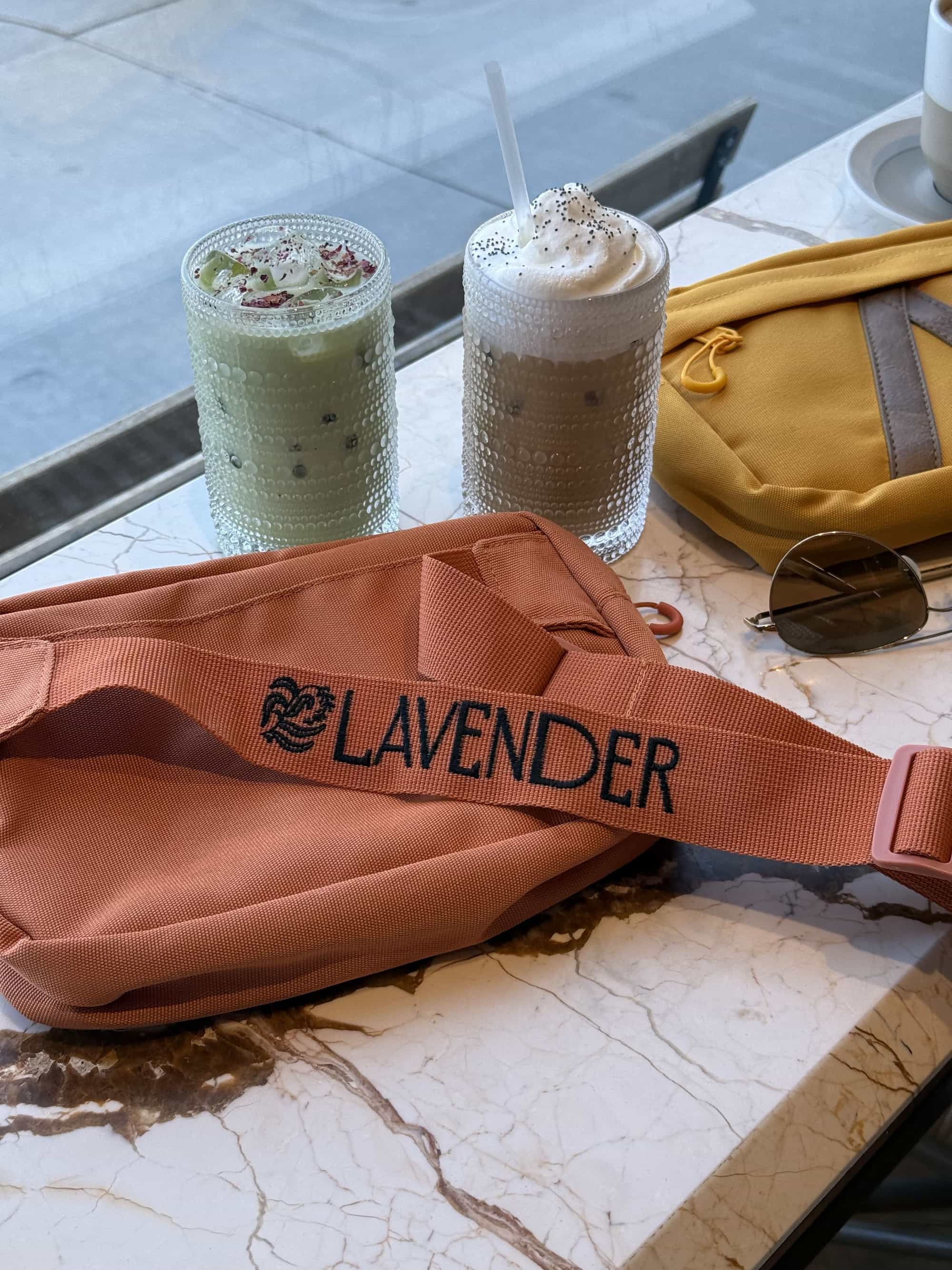 Fanny pack, yellow, with lavender logo, on marble table with drinks