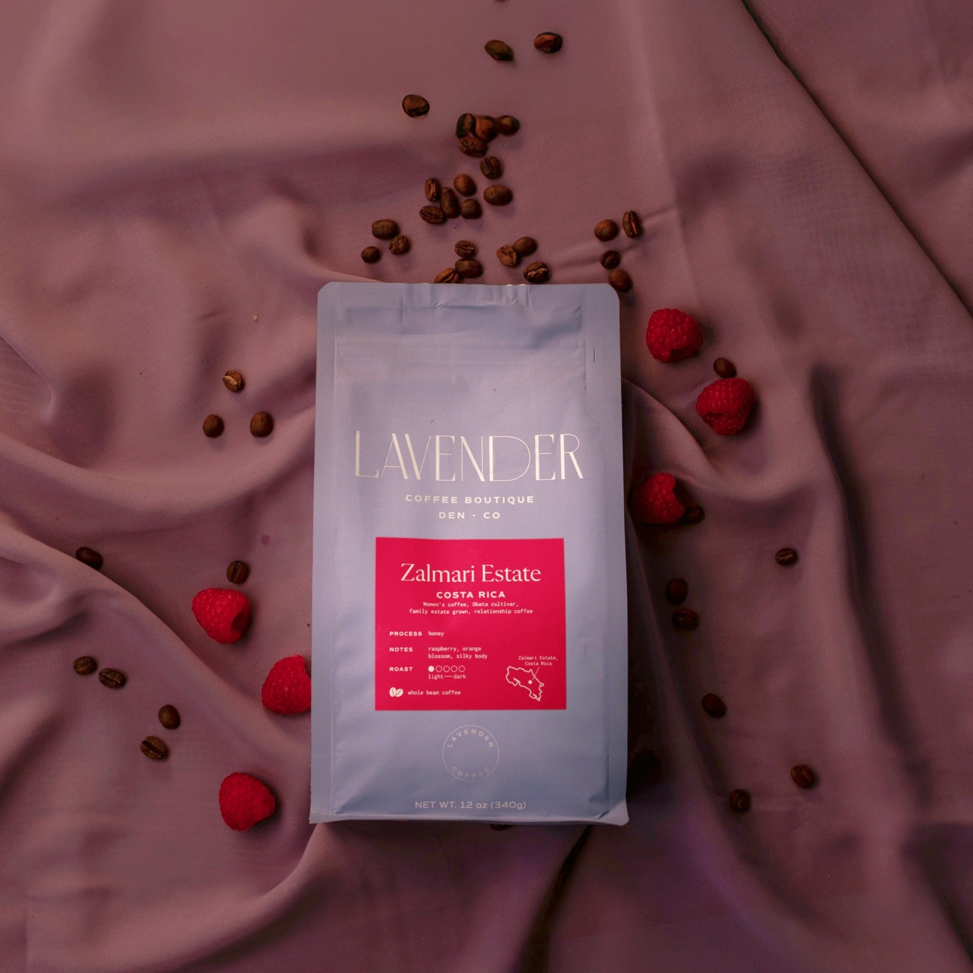 Coffee package with red label on a pink fabric background with coffee beans and red berries.