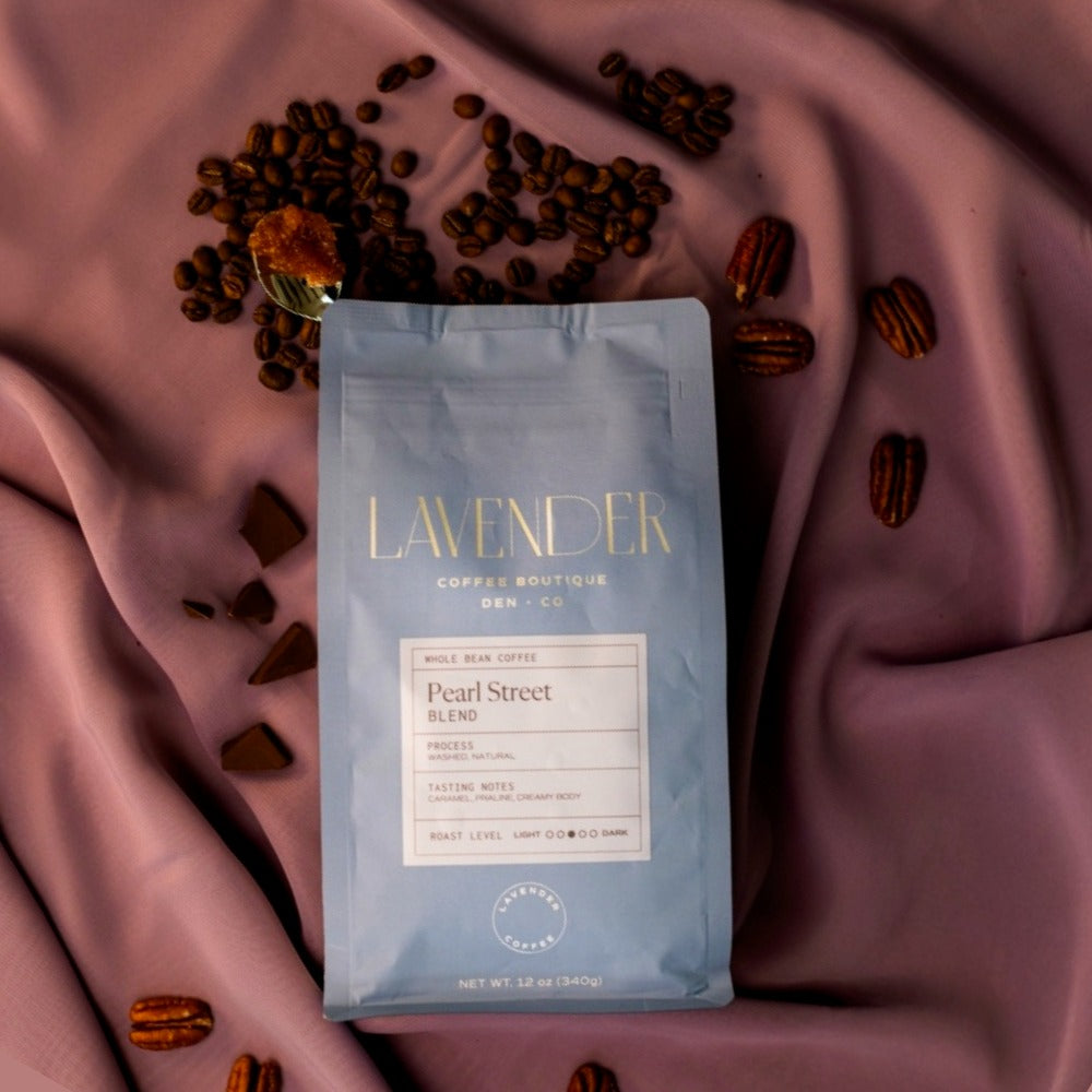 Lavender Coffee Boutique Pearl Street Blend coffee package on a pink fabric background with coffee beans.