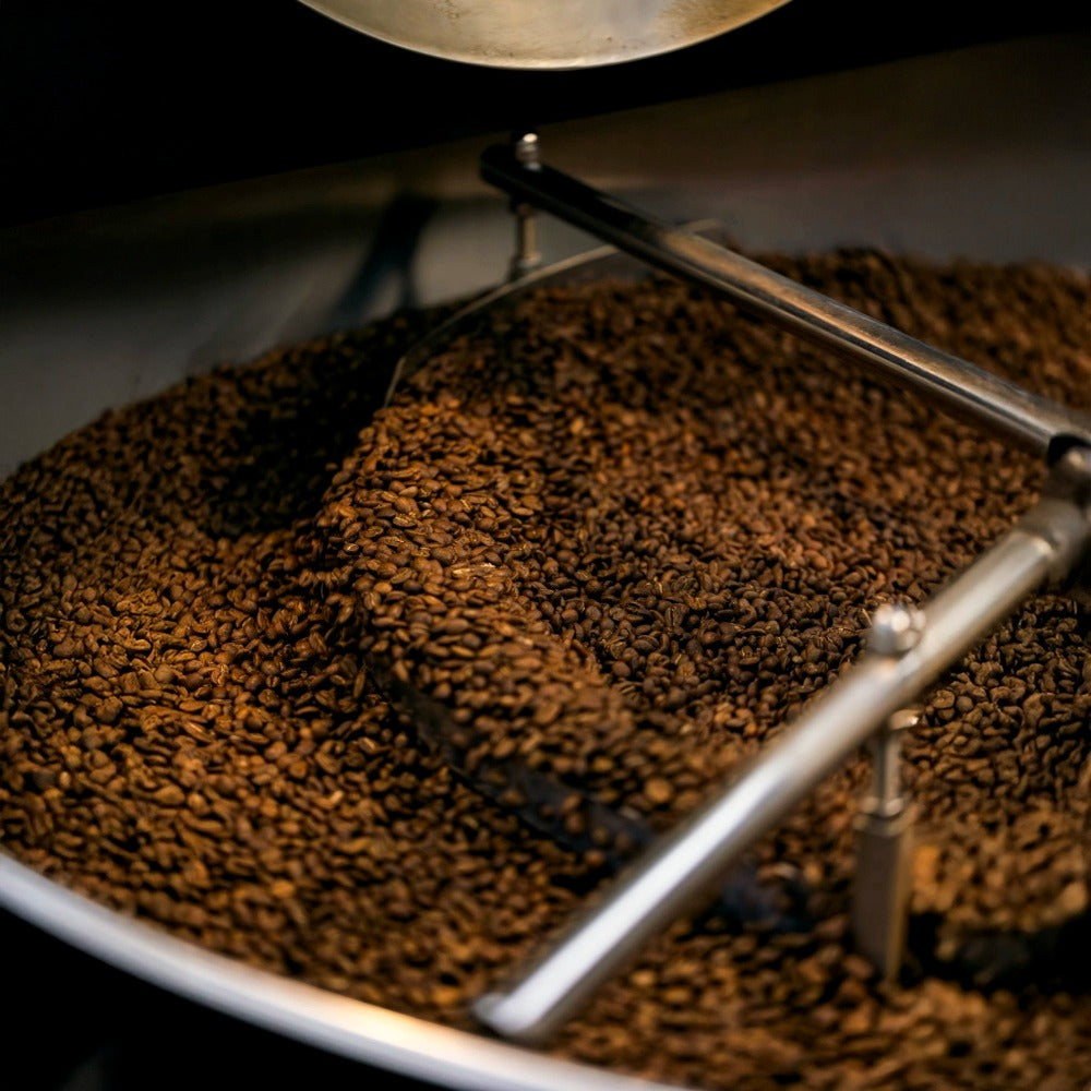 Coffee beans in a roasting machine with a metal scoop