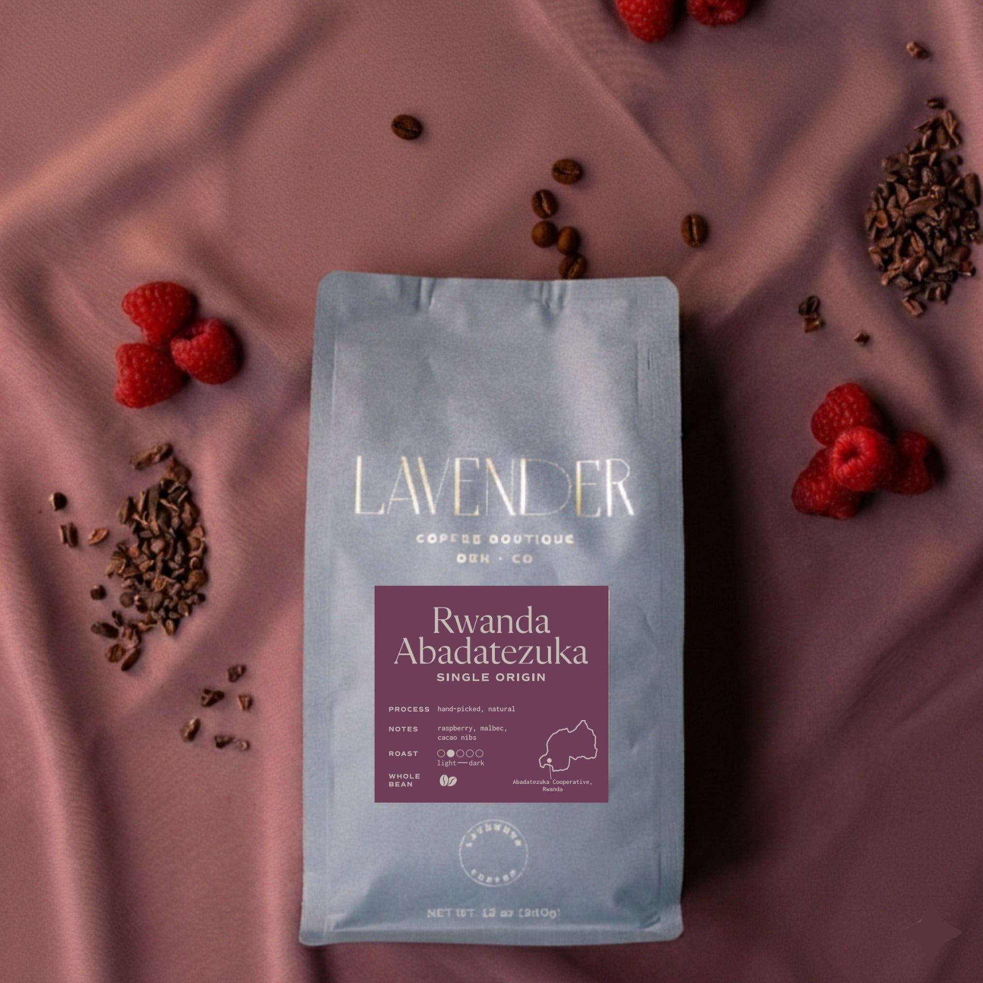 Lavender Coffee Boutique Rwanda Abadatezuka single origin coffee bag with raspberry and cacao nibs on a purple fabric background
